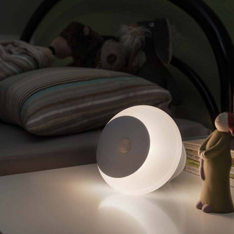 LED Nachtlicht Viby mit Dämmerungssensor 3000K Weiß auf einem Nachttisch neben einem Spielzeug.
