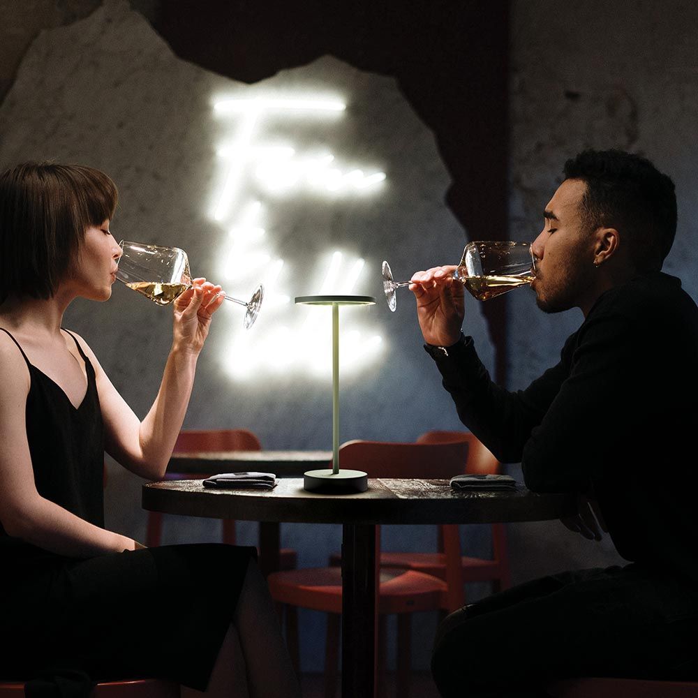 Zwei Personen genießen Wein an einem Tisch mit der LED Outdoor Akku-Tischlampe Smart im Hintergrund.