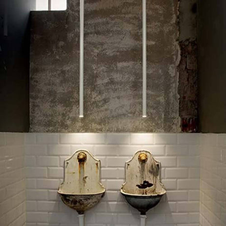 Zwei vintage Toiletten mit Rost auf einem weißen Fliesenboden, beleuchtet von LED-Leuchten an der Wand.