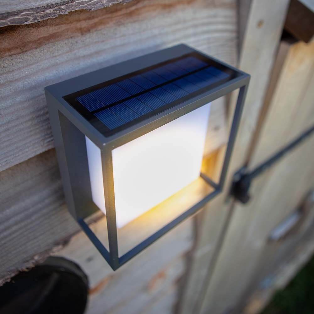 LED-Solar-Außenleuchte Curtis mit Bewegungsmelder an einer Wand montiert, mit solarem Ladepanel.