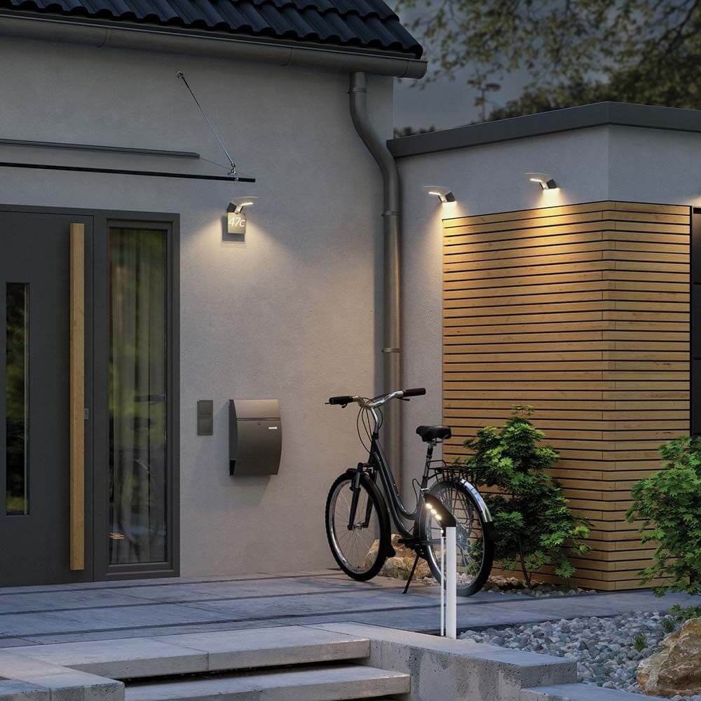 Moderne Eingangsszene mit LED Solar Pollerleuchte Soley, Fahrrad und stilvoller Hausfassade bei Dämmerung.