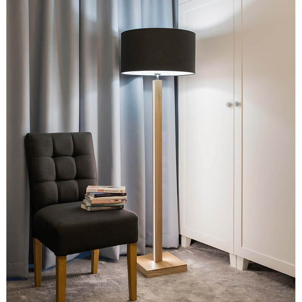 LED Stehlampe Asseto 3350lm Eiche-Geölt, Schwarz neben einem Stuhl in einem modernen Wohnzimmer.