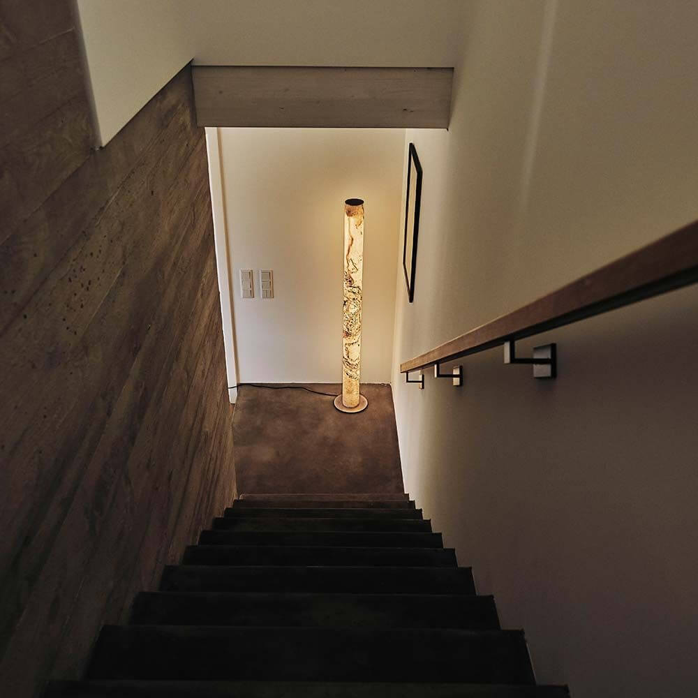 LED Stehleuchte Columna aus Stein Weißperle im Treppenhaus, minimalistische Gestaltung und warmes Licht.
