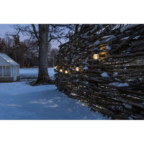 LED Sturmlaternen Lichterkette 8 grüne Sturmlaternen 8 Warmweiße Dioden IP44 an einem Holzzaun im Schnee.