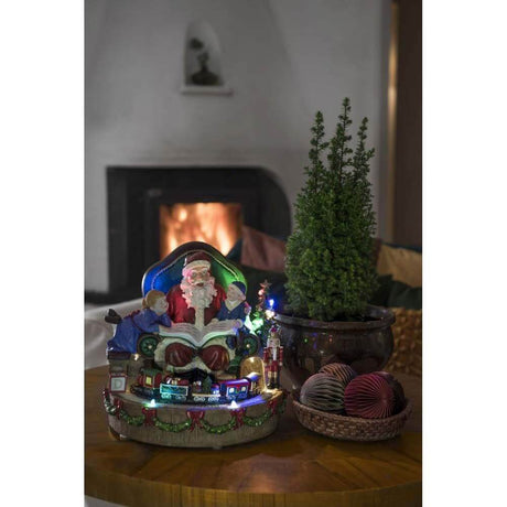 LED Santa Claus with children and train Christmas carols battery-operated indoors on a table with plants in the background.