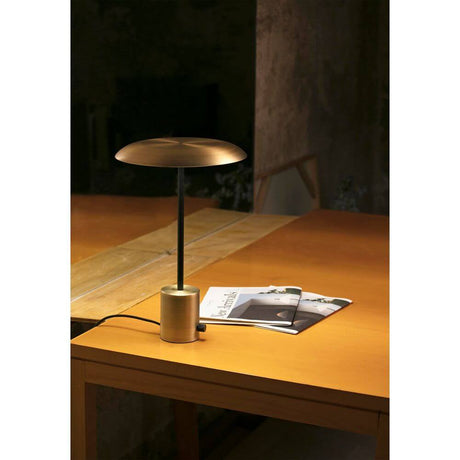 LED Tischlampe HOSHI Goldfarben-Satin, Schwarz auf einem Tisch mit einer Zeitschrift.