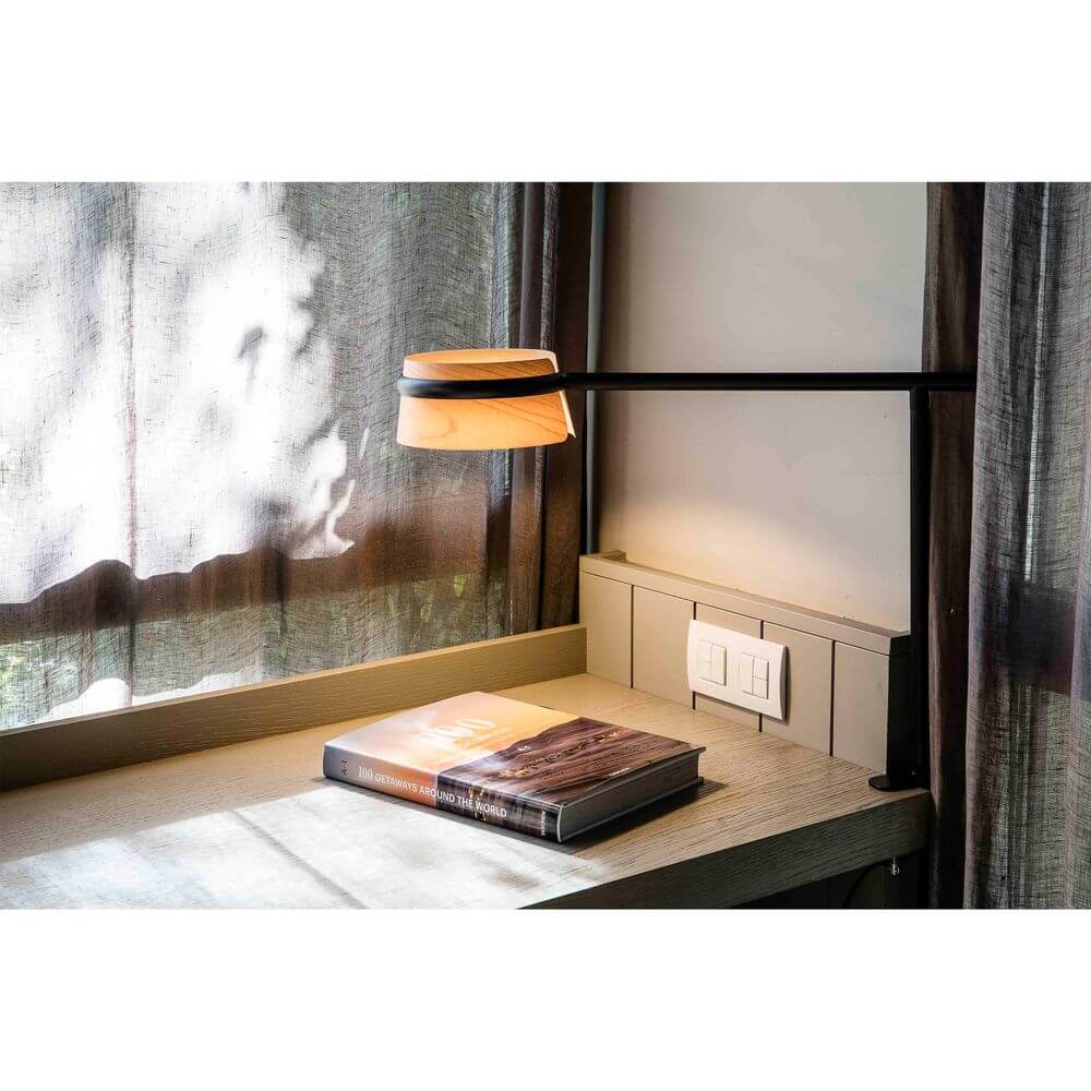 LED Tischlampe LOOP Schwarz, Braun auf einem Tisch mit einem Buch und Stromanschlüssen im Hintergrund.