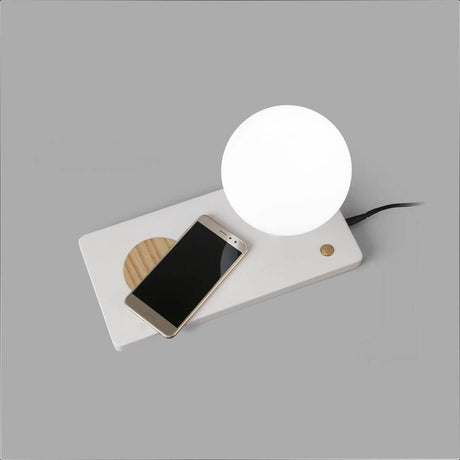 LED Tischleuchte NIKO mit induktiver Handy Ladestation und Smartphone auf Tischplatte.