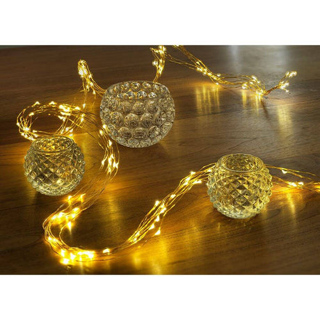 LED Drop tinsel 24 strands with 20 diodes 480 warm white diodes gold-colored wire on table with glass candle holders.