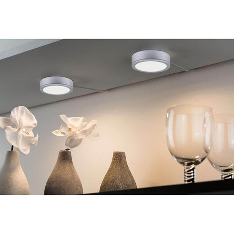 LED Unterschrankleuchte Pukk Chrom-Matt an einem Regal mit Blumen und Gläsern.