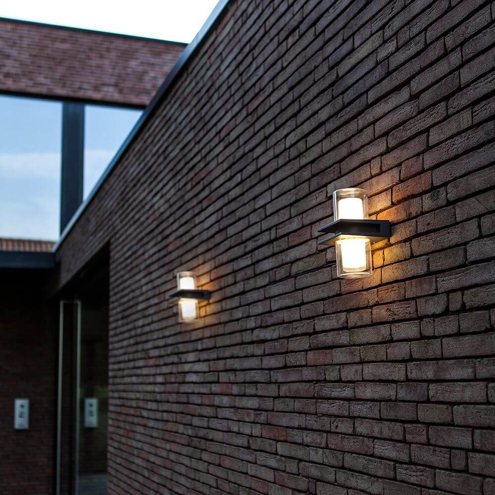 LED Außenwandlampe Tango IP44 Anthrazit an einer Backsteinwand montiert, strahlt helles Licht nach oben und unten aus.
