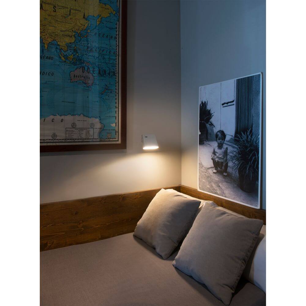 LED Wandleuchte AUREA 6W 2700K Weiß an einer Wand über einem Bett mit Kissen und Kunstwerk.