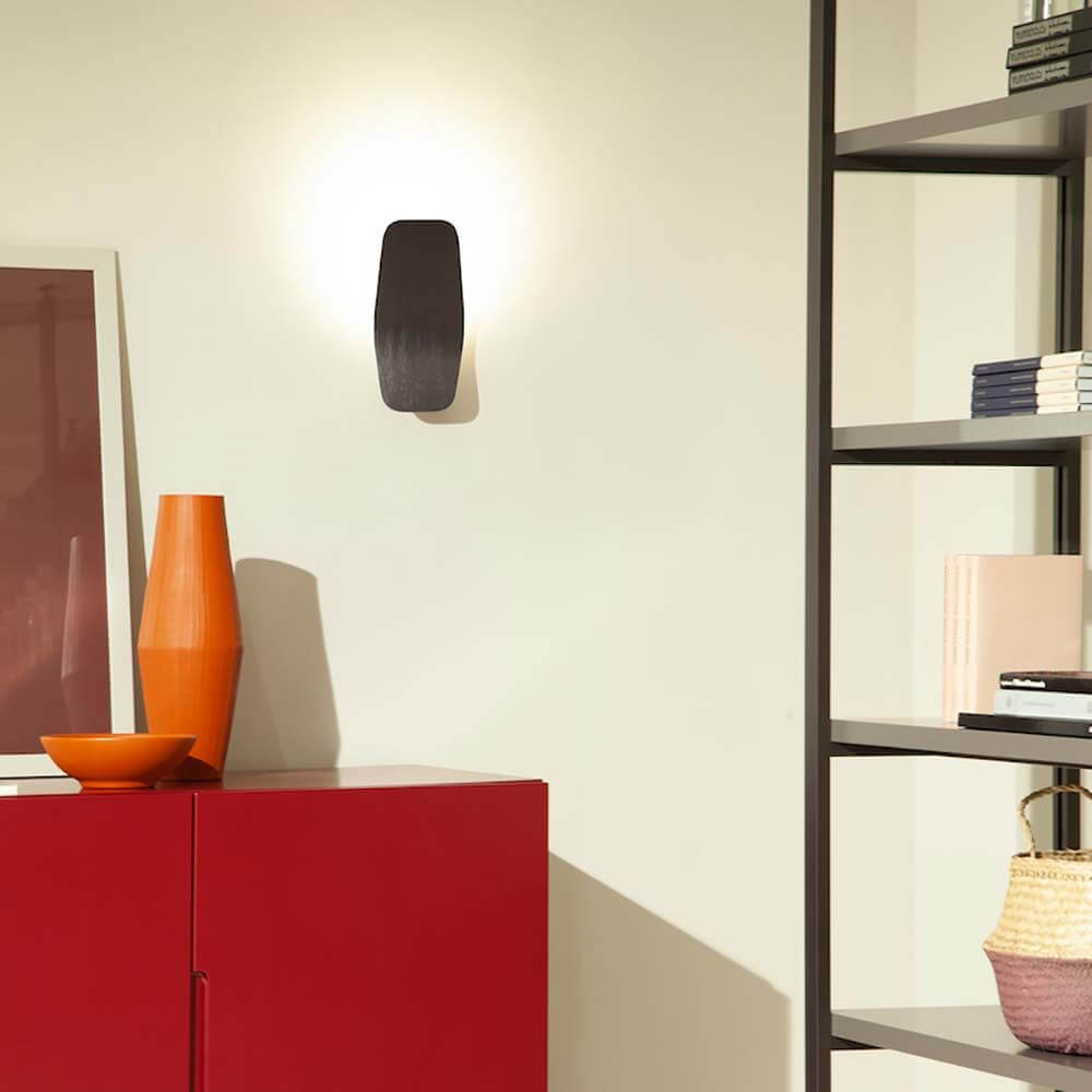 LED-Wandleuchte Ashiya in elegantem Design, an einer Wand neben modernen Dekoobjekten und Regalen.