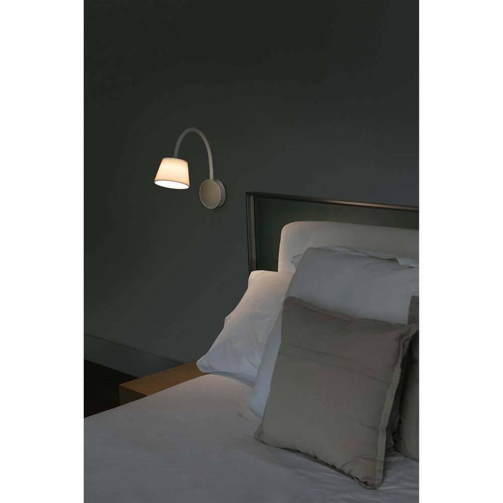 LED Lese-Wandleuchte BLOME Weiß an einer Wand neben einem Bett mit Kissen.