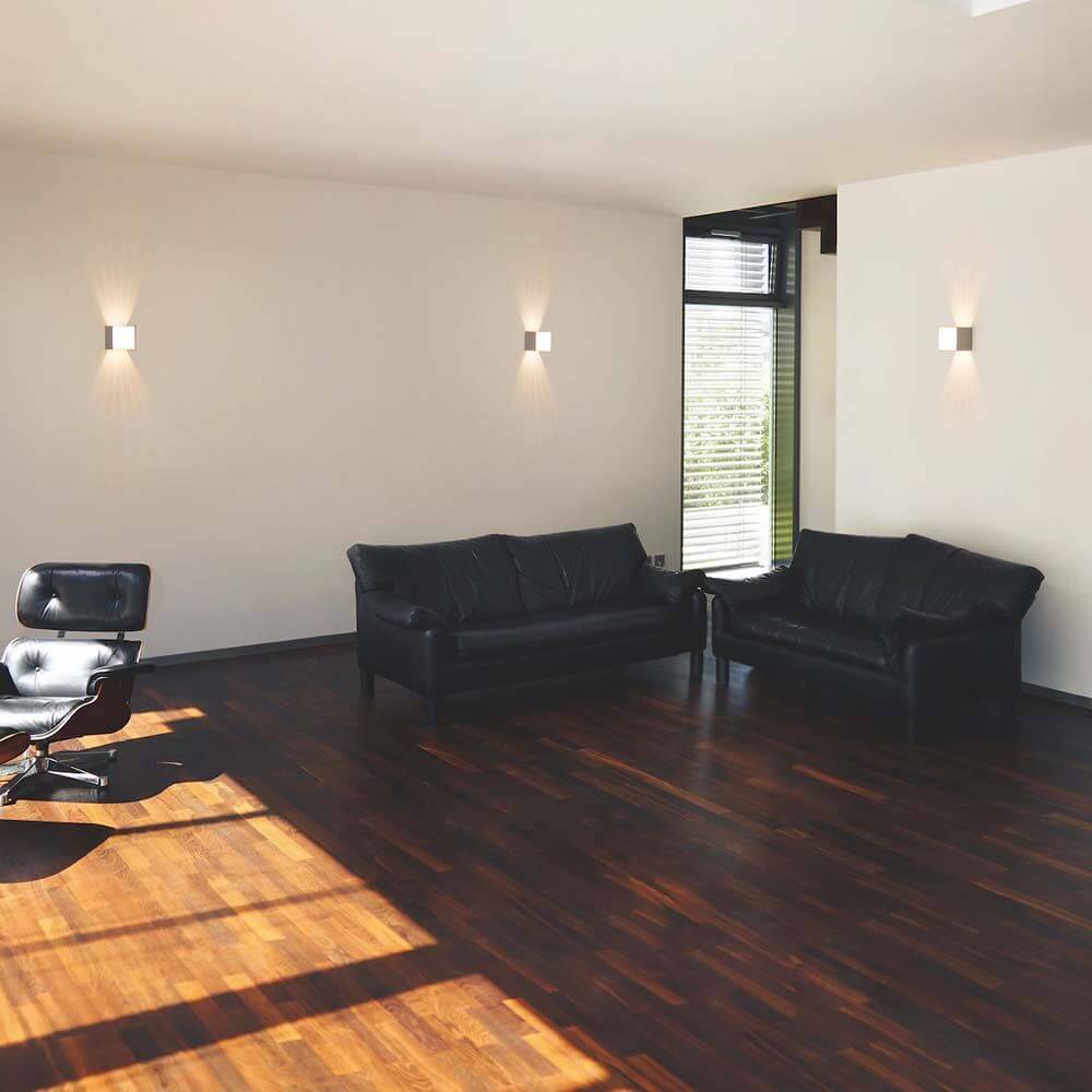 Casablanca LED-Wandleuchte Box in modernem Wohnraum mit Holzfußboden und schwarzen Sofas.