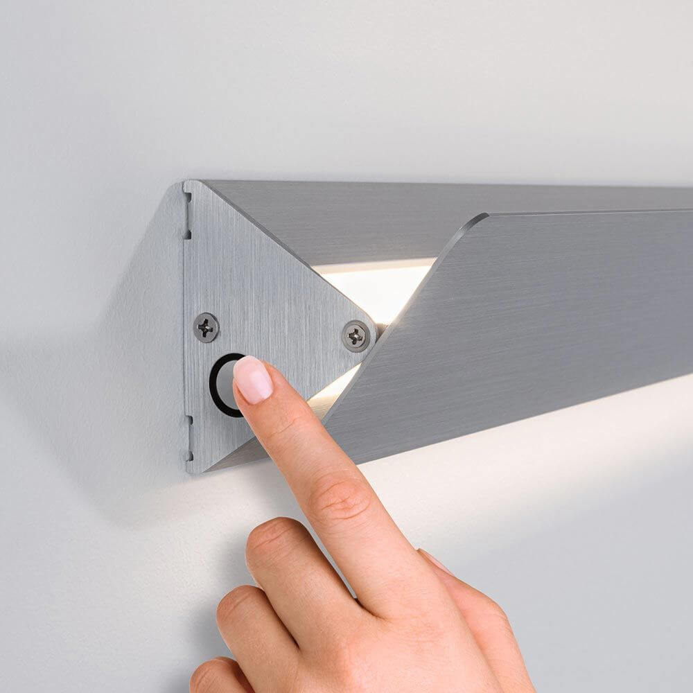 Detailaufnahme der LED Wandleuchte Katla Metall 60cm mit einem Finger, der den Schalter betätigt.
