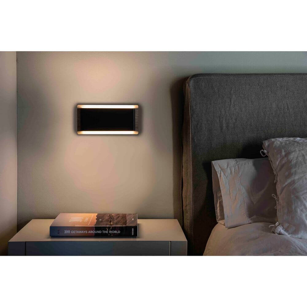 LED Wandleuchte MOOD 2x3W Braun, Schwarz an einer Wand neben einem Bett und Nachttisch.