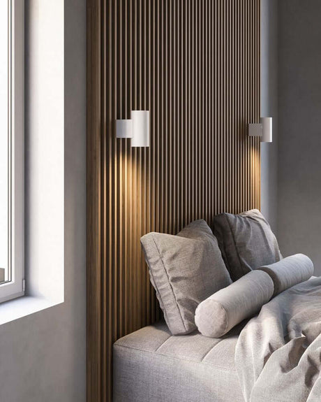 LED Mona væglampe placeret på en væg over en moderne seng med puder.