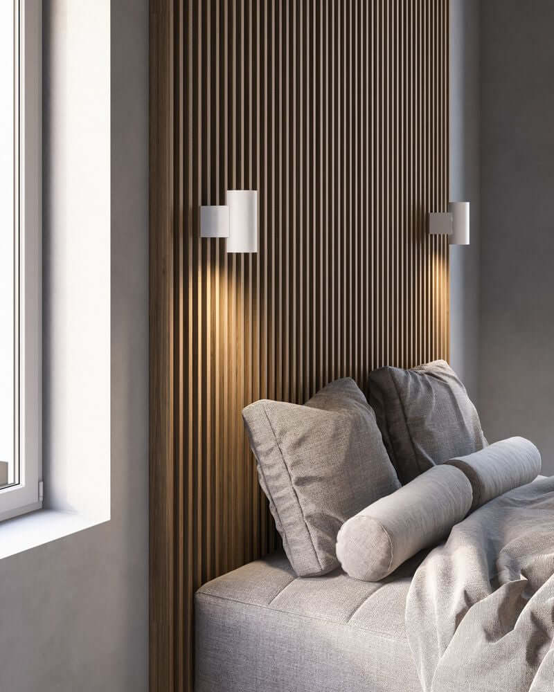 LED Wandleuchte Mona an einer Wand über einem modernen Bett mit Kissen platziert.