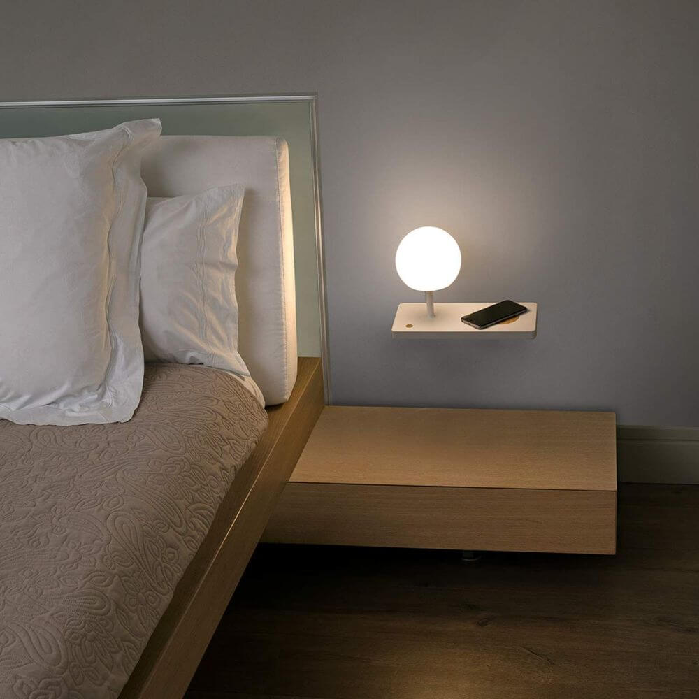 LED Wandleuchte NIKO Links Weiß, Braun neben einem modernen Bett mit Kissen und Mobiltelefon.