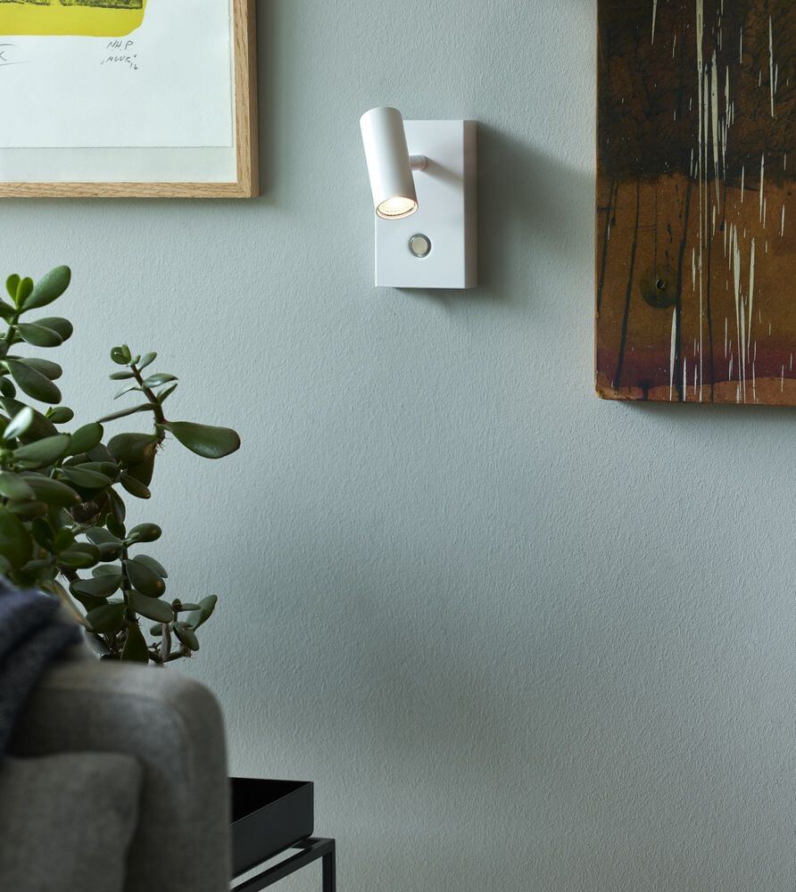 Minimalistische LED Wandleuchte Omari in Weiß mit Touch-Dimmer, an einer Wand neben einer Pflanze.