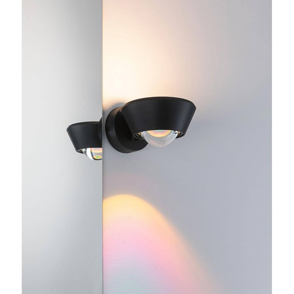 LED Wandleuchte Sabik Dimmbar Schwarz an einer Wand mit Regenbogenlichtakzenten.