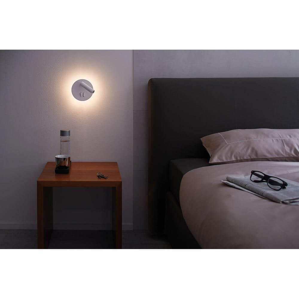 LED Wandleuchte Tabari Weiß, Chrom an einer Schlafzimmerwand über einem Holztisch.