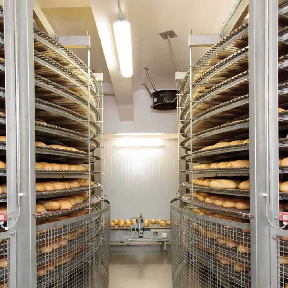 Blick in eine Industrielle Bäckerei mit Regalen voller frisch gebackener Brötchen und LED-Wannenleuchte.