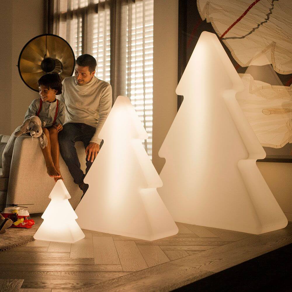 Familie genießt beleuchtete Weihnachtsbaum-Dekoration im Wohnzimmer, in warmem Licht.