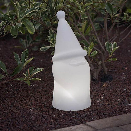 LED Christmas gnome Amelio battery + solar IP65 glowing in the garden among plants.