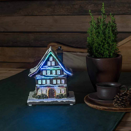 LED Battery-operated winter house & 3 multicolored LEDs on a table with a plant and a cup.