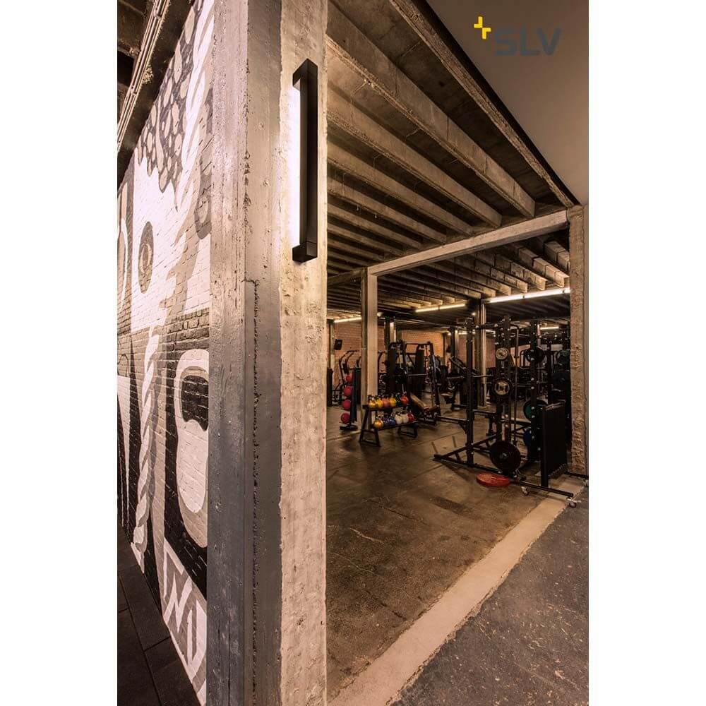 Long Grill LED Wand- und Deckenleuchte Schwarz 3000K an Wand in modernen Fitnessstudio-Umgebung.