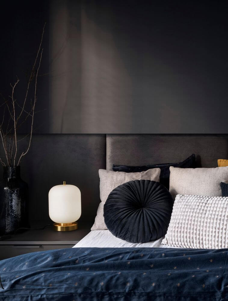 Moderne Schlafzimmeransicht mit schwarzer Tischleuchte, dekorativen Kissen und stilvollem Bettzeug.