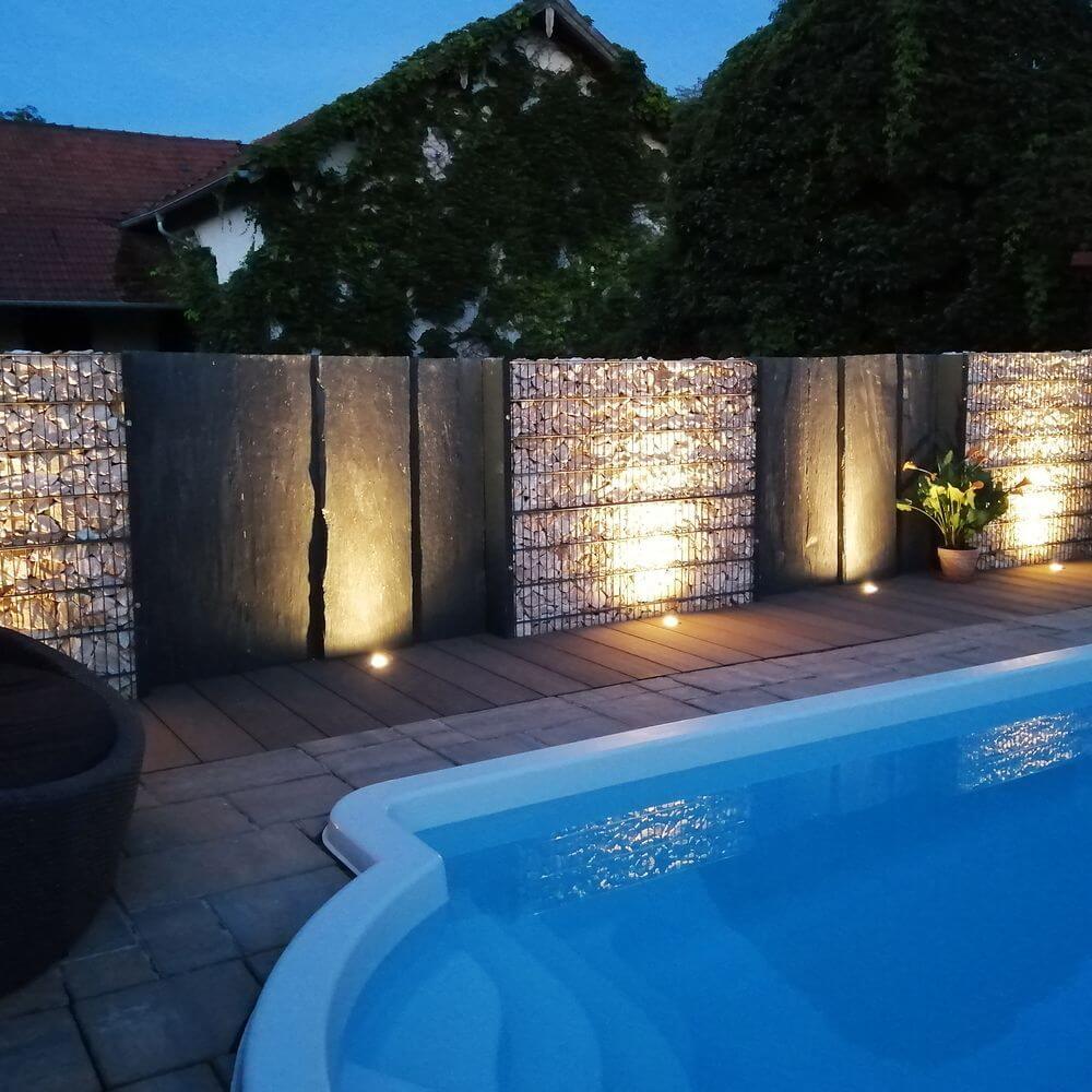 Eingebauter Bodeneinbaustrahler beleuchtet Poolbereich mit Steinmauern und Pflanzen bei nacht.