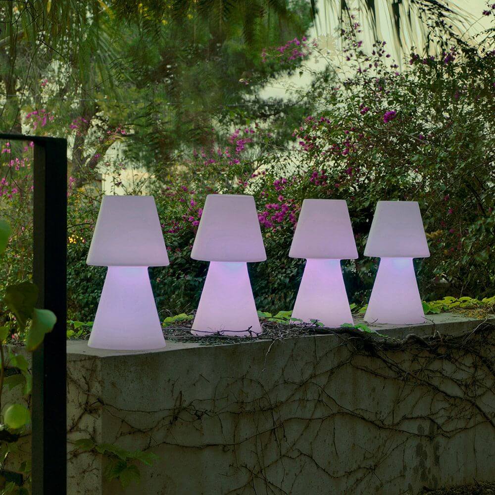 LED-Akku-Tischleuchte Lola Large mit Fernbedienung im Freien, stilvoll beleuchtet vor buntem Blumenhintergrund.