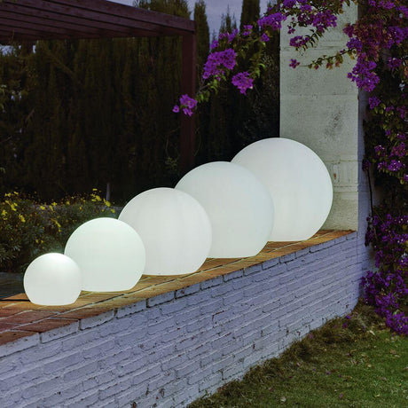 Buiten-decoratieverlichting Buly Ø 30cm in verschillende maten op een muur in de tuin.