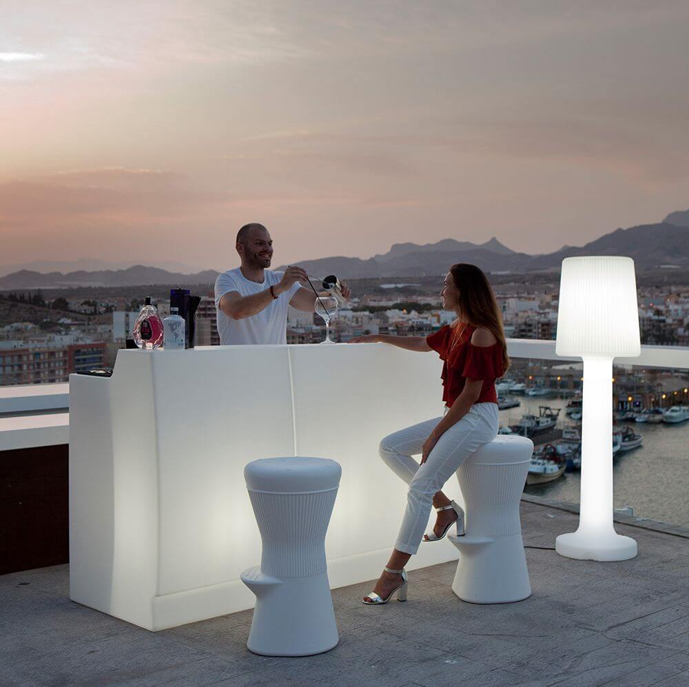 Moderne Außen-Stehleuchte Carmen 165cm mit eleganten Bar-Möbeln bei Sonnenuntergang am Hafen.