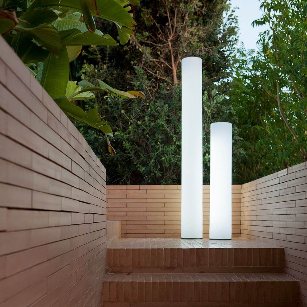 Säulenförmige Außen-Stehleuchten Fity Big leuchten in einem Garten, umgeben von grünem Pflanzen backdrop.