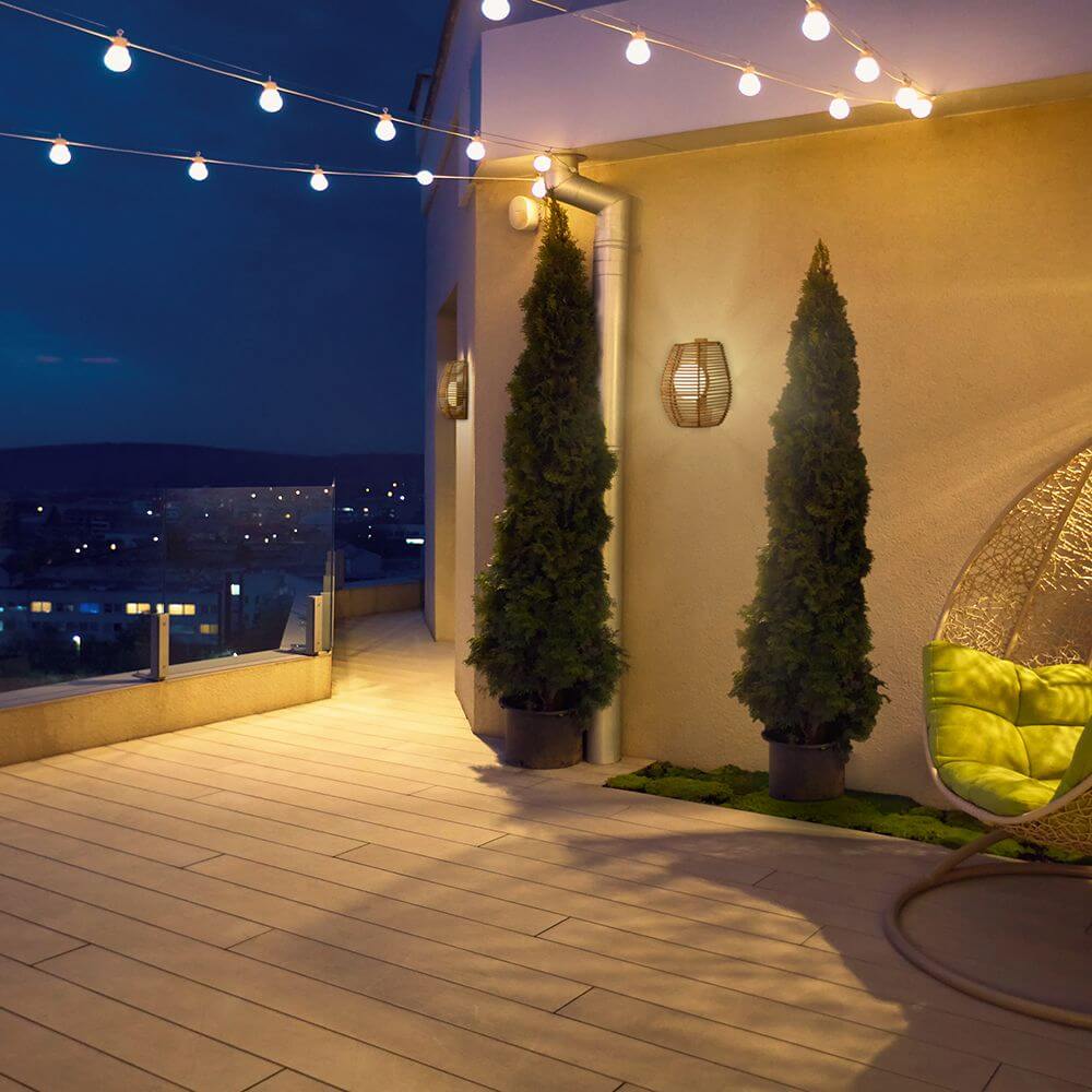 Bossa Boho-Style Akku-Außenwandlampe Rattan IP54 Boho-Style an einer stilvollen Terrasse bei Nacht.