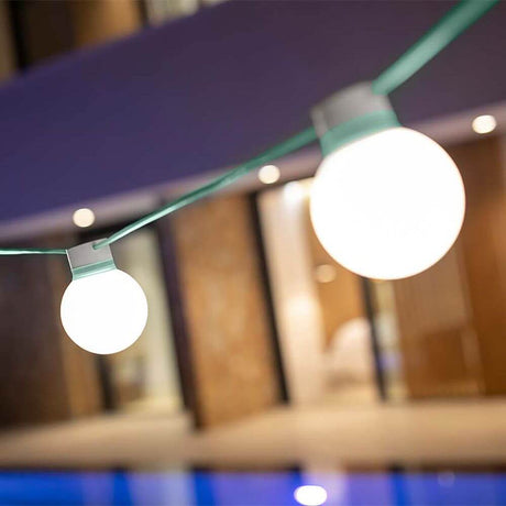 Bruna LED beer garden string lights 8 m with glowing globe lamps in a garden setting.