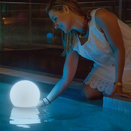Buly LED Solar ball light White with remote control floats in the water while a woman touches it.