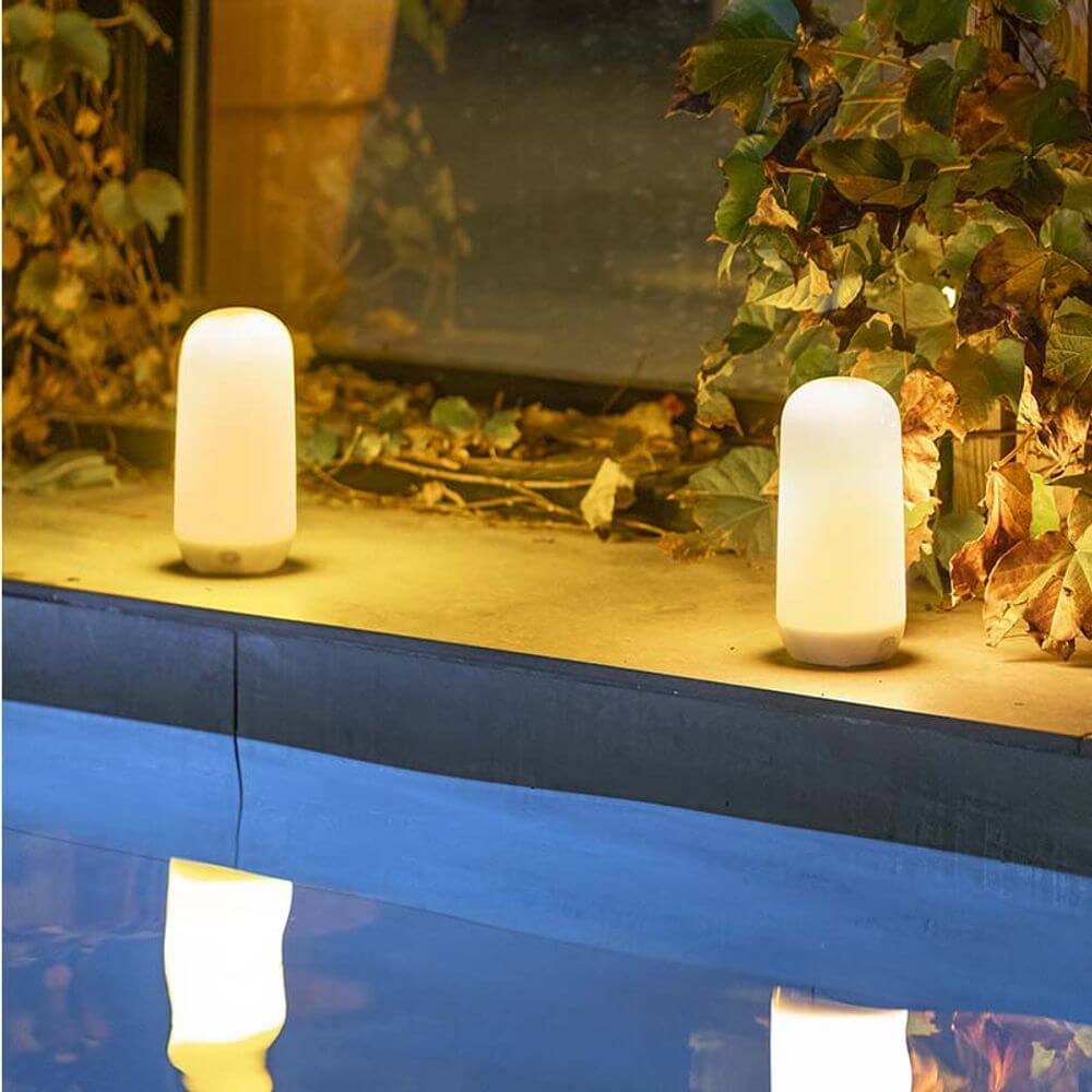 Wiederaufladbare Candy Akku-Tischleuchte mit sanftem Flammen-Effekt am Pool, umgeben von Pflanzen.