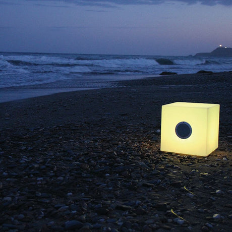 LED Decorative Cuby table with speaker and remote control on the beach, atmospheric lighting at night.
