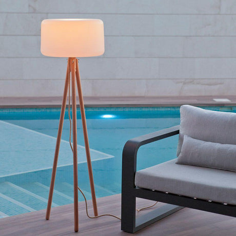 Candeeiro de pé tripé LED Chloe com bateria e comando à distância ao lado de um sofá moderno junto à piscina.