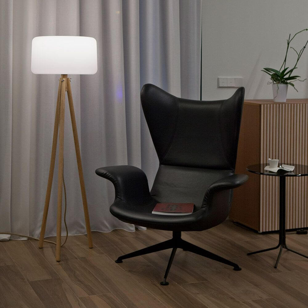 Dreibein LED-Stehleuchte Chloe mit Akku und Fernbedienung neben einem modernen Sessel in stilvollem Innenraum.