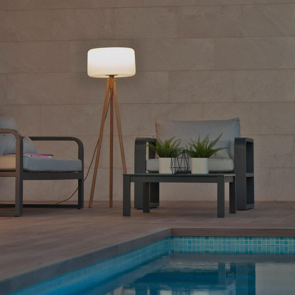 Dreibein LED-Stehleuchte Chloe mit Akku und Fernbedienung neben einem Pool auf einer Terrasse.