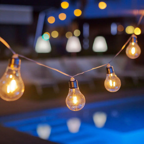 Wireless Stella Solar garland, 10-light, with glowing bulbs over a pool at night.