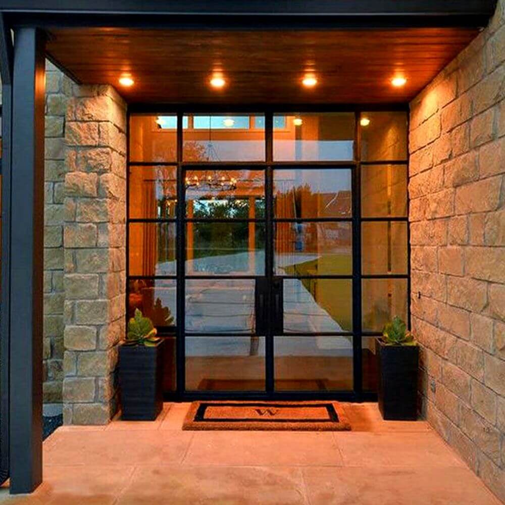 Moderne Eingangstür mit großem Fenster und Außenlichtern, umgeben von Steinmauern und Topfpflanzen.