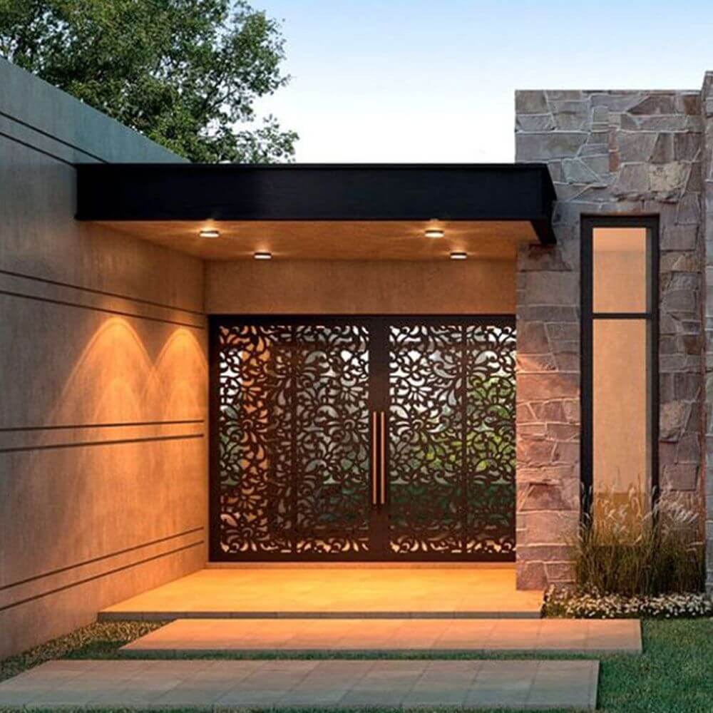 Moderne Außeneingangstür aus Metall mit floralen Mustern, umgeben von Stein und LED-Beleuchtung.