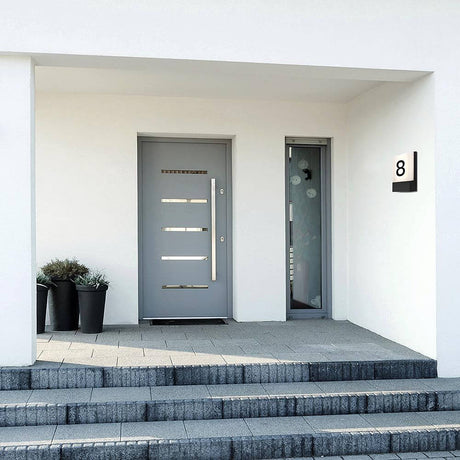 Modern entrance portal with a grey door, white walls and planters along the path.
